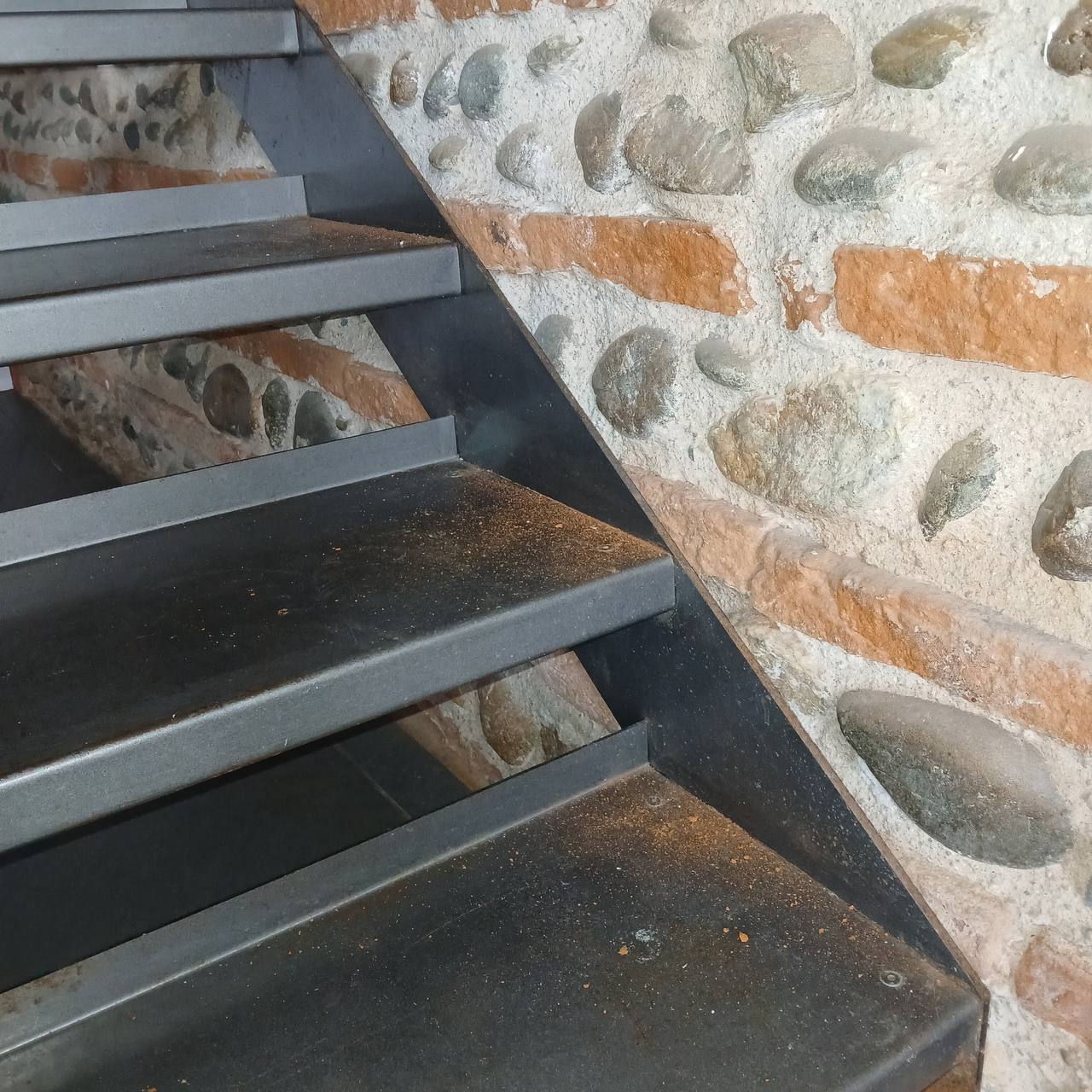 Mur de briques foraine et galets sous escalier métallique — état brut, avant traitement